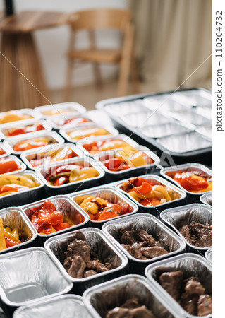 Meal Prep Service: Portioning Healthy Meat and Vegetables. A meal prep worker portions nutritious beef and colorful bell peppers into individual trays, preparing well-balanced office lunches. Meal Prep Service: Portioning Healthy Meat and Vegetables. A meal prep worker portions nutritious beef and colorful bell peppers into individual trays, preparing well-balanced office lunches. 110204732