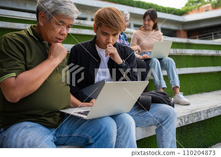 Focused young students listening old senior aged teachers for advise capstone project in university. Happy middle aged teacher working together with students for graduation project. 110204873