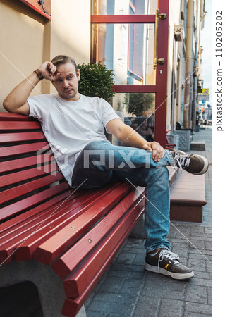 a man on a walk outside in the summer sits on a red bench. sunny day a man on a walk outside in the summer sits on a red bench. sunny day 110205202