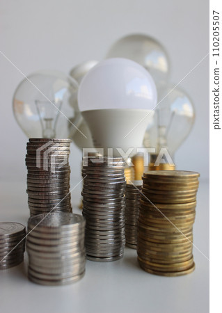 Variety Electric Bulbs And Piles Of Silvery And Brass Coins In A Columns Symbolizing Energy Efficient Variety Electric Bulbs And Piles Of Silvery And Brass Coins In A Columns Symbolizing Energy Efficient 110205507