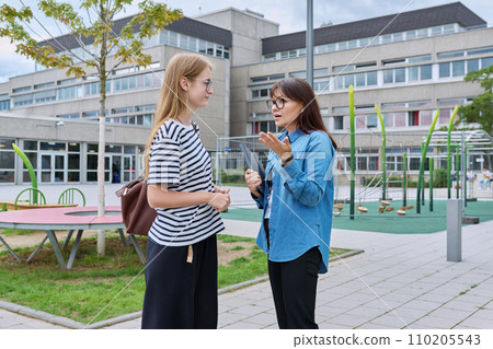 Talking teacher and teenage schoolgirl outdoor, school building background 110205543