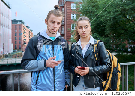 Outdoor portrait of teenagers students, smiling guy and girl with backpack looking at camera 110205574