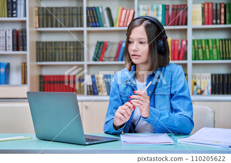 Female college student in headphones with laptop having online video chat, inside library Female college student in headphones with laptop having online video chat, inside library 110205622