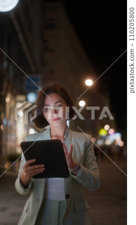 Vertical view of the beautiful young woman using tablet computer while walking through night city 110205800