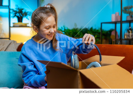 Happy child girl shopper unpacking cardboard box delivery parcel online shopping purchase at home 110205834