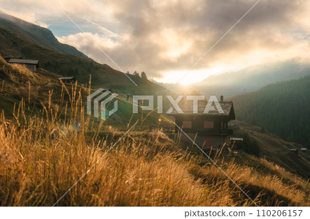 Sunrise shines over wooden cottage on hill among the Swiss Alps in mountain village at Switzerland Sunrise shines over wooden cottage on hill among the Swiss Alps in mountain village at Switzerland 110206157