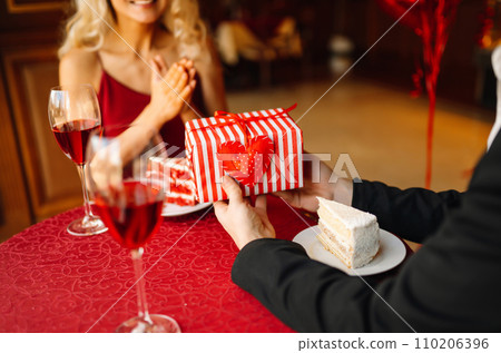Couple in love exchanges gifts for Valentine's Day in a cafe at the table. Concept of holiday, love. 110206396