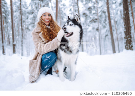 Beautiful young woman plays with her dog in winter forest. First snow Friendship. Outdoor recreation 110206490