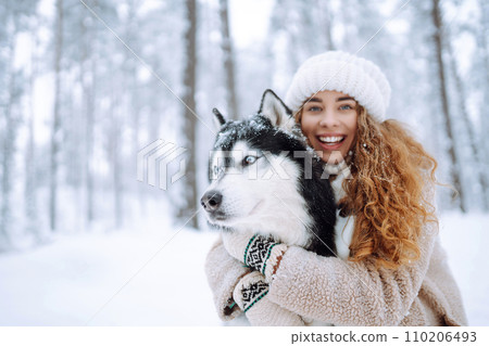 Beautiful young woman plays with her dog in winter forest. First snow Friendship. Outdoor recreation 110206493