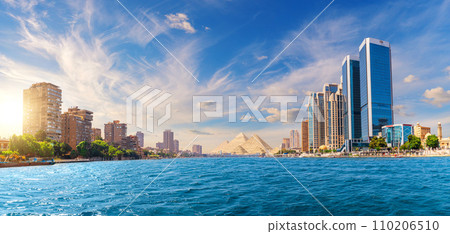 Unique panorama of the Nile river, modern buildings and famous Pyramids of Giza, Cairo, Egypt Unique panorama of the Nile river, modern buildings and famous Pyramids of Giza, Cairo, Egypt 110206510