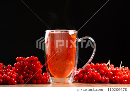 Hot viburnum tea in a glass cup with a double bottom on a black background. Hot viburnum tea in a glass cup with a double bottom on a black background. 110206678