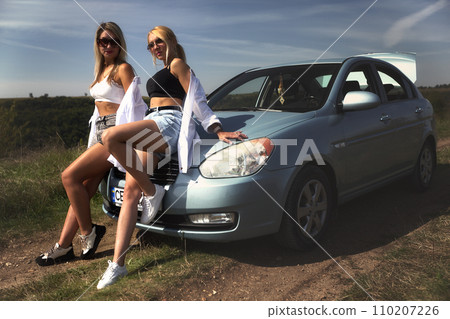 skinny girls are relaxing near a broken car away from the bustle of the city, best friends are free and enjoy the journey. High quality photo 110207226
