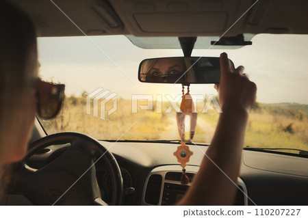 A beautiful girl rides in a car at speed and looks in the rear-view mirror, rest from work and bustle, serenity and freedom. Escape from problems and a chance to be alone. High quality photo 110207227