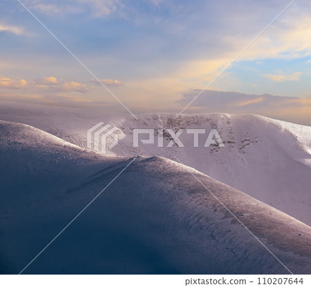 Snow covered winter mountains  in last evening sunlight. Magnificent windy dusk on tops above picturesque alpine ski resort 110207644