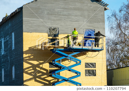 Residential house facade painting works after cladding with wooden planks using scissor lift platform 110207794