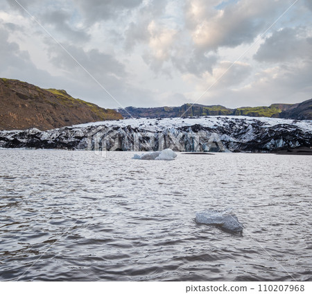 Solheimajokull picturesque glacier in southern Iceland. The tongue of this glacier slides from the volcano Katla. Beautiful glacial lake lagoon with blocks of ice and surrounding mountains. 110207968