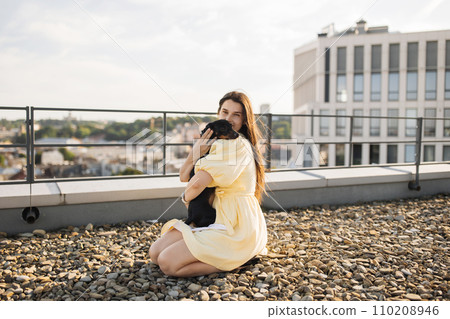 Attractive lady sitting on ground and hugging dog on roof 110208946