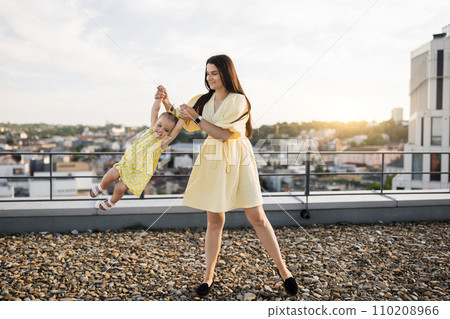 Adult lady holding and spinning with kid on city roof 110208966