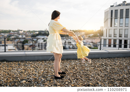 Adult lady holding and spinning with kid on city roof 110208971