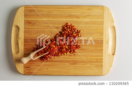 Spoon with crushed dry red chili peppers on a wooden kitchen board. Spoon with crushed dry red chili peppers on a wooden kitchen board. 110209365