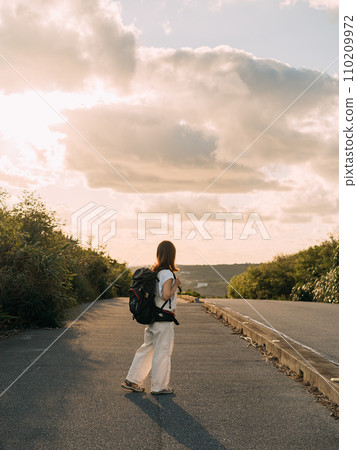A woman walking toward the setting sun 110209972