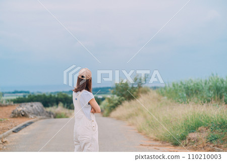 A woman walking through a sugar cane field leading to the sea 110210003