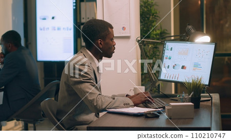 Experienced employee arriving at work, sitting at office desk ready to imput data on computer during nightshift. Meticulous bookkeeper in workspace typing datasets, working overnight 110210747
