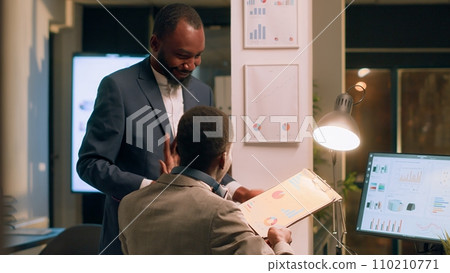 Friendly manager trying to make employee with headphones on pay attention at work in office. Management executive giving task to worker listening to music during nightshift Friendly manager trying to make employee with headphones on pay attention at work in office. Management executive giving task to worker listening to music during nightshift 110210771