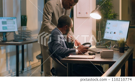 Management executive interrupting worker listening to music slacking in office to show him mistake he needs to fix. Employee taking headphones off after being given tasks to do by supervisor Management executive interrupting worker listening to music slacking in office to show him mistake he needs to fix. Employee taking headphones off after being given tasks to do by supervisor 110210774