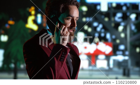Businessman on phone call strolling around city, enjoying night walk while he talks on smartphone. Person admiring skyscrapers, walking near busy town center district on promenade. Handheld shot. Businessman on phone call strolling around city, enjoying night walk while he talks on smartphone. Person admiring skyscrapers, walking near busy town center district on promenade. Handheld shot. 110210800