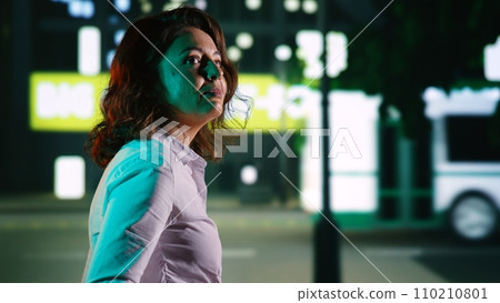 Young woman walking around town at night, going out for relaxing promenade under streetlights. Person strolling near city center downtown district, admiring buildings and skyscrapers. Handheld shot. Young woman walking around town at night, going out for relaxing promenade under streetlights. Person strolling near city center downtown district, admiring buildings and skyscrapers. Handheld shot. 110210801