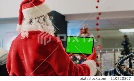 Christmas ornate shopping mall employee impersonating Santa Claus holding mockup tablet, taking a break from job to watch videos on chroma key screen while clients walk around, close up 110210807