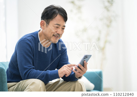 一名 50 多歲的男子坐在沙發上操作智慧型手機 110212840