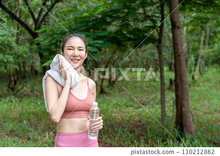 Young attractive Asian woman wiping off her sweat from her forehead during her water break from her morning exercise run at a running track of a local park 110212862