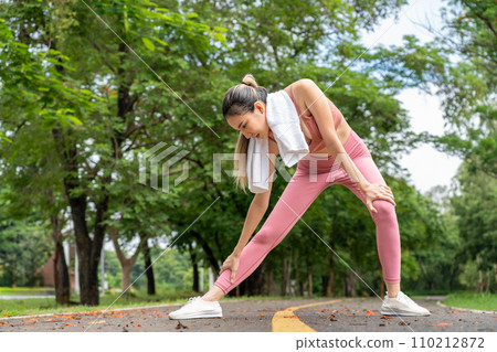 Young attractive Asian woman stretching her arms and legs before her morning exercise run at running track of a local park 110212872