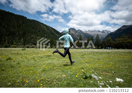Woman trail runner cross country running in high altitude flowering mountains 110213512