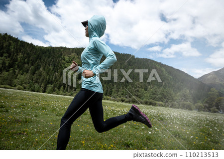 Woman trail runner cross country running in high altitude flowering mountains 110213513