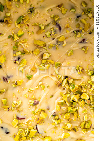 Filling square cheesecake pan lined with parchment paper with fudge mixture to prepare cranberry pistachio fudge. 110215310