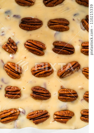 Pouring fudge mixture into the baking pan lined with parchment paper to prepare white chocolate cranberry pecan fudge. 110215339