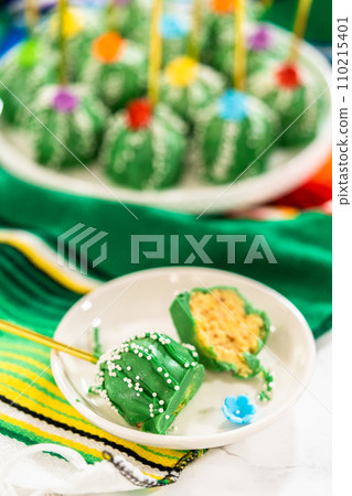 Cactus-shaped cake pops, beautifully decorated with luster dust, sugar flowers, and white sprinkles, arranged in celebration of Cinco de Mayo. 110215401