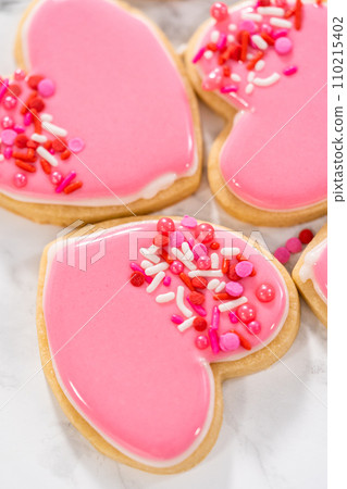 Decorating heart-shaped sugar cookies with pink and white royal icing for Valentine's Day. 110215402