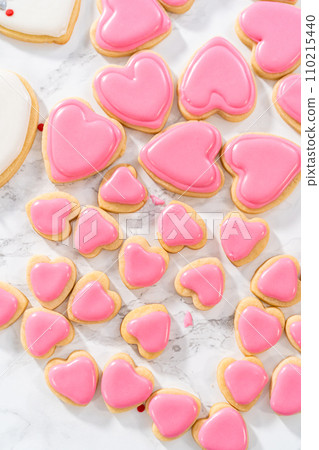 Decorating heart-shaped sugar cookies with pink and white royal icing for Valentine's Day. Decorating heart-shaped sugar cookies with pink and white royal icing for Valentine's Day. 110215440