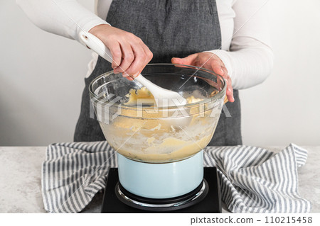 Melting white chocolate chips and other ingredients in a glass mixing bowl over boiling water to prepare cranberry pistachio fudge. 110215458