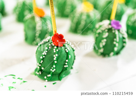 Cactus-shaped cake pops, beautifully decorated with luster dust, sugar flowers, and white sprinkles, arranged in celebration of Cinco de Mayo. 110215459