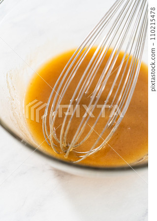 Mixing wet ingredients in a small glass mixing bowl to bake gingerbread bundt cake with caramel filling 110215478