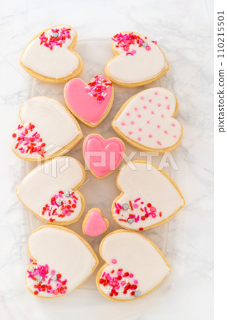 Storing heart-shaped sugar cookies with pink and white royal icing in a large plastic container. Storing heart-shaped sugar cookies with pink and white royal icing in a large plastic container. 110215501