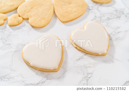 Decorating heart-shaped sugar cookies with pink and white royal icing for Valentine's Day. Decorating heart-shaped sugar cookies with pink and white royal icing for Valentine's Day. 110215582