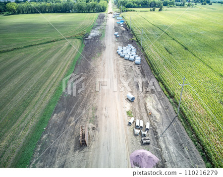 High angle view of a road construction project cutting through an agricultural district of farm fields. 110216279