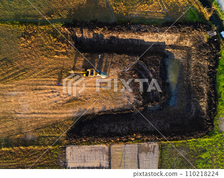 Excavating dirt into a dump truck to build a water storage pond for use in the dry season for agriculture. Aerial view of a backhoe is working. Excavating dirt into a dump truck to build a water storage pond for use in the dry season for agriculture. Aerial view of a backhoe is working. 110218224