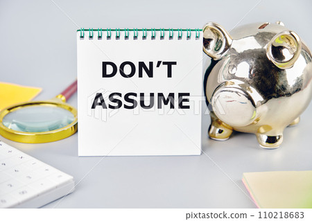 DO NOT ASSUME A word, a text written on a notebook next to a piggy bank, a magnifying glass, a calculator, stickers 110218683